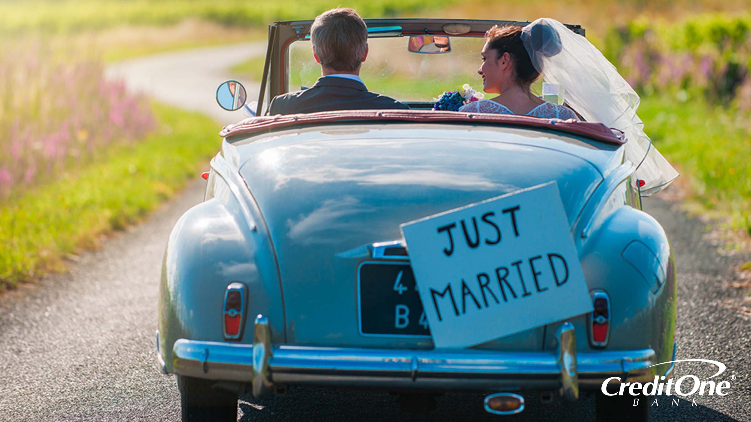 A newly married couple driving away together with a 'Just Married' sign